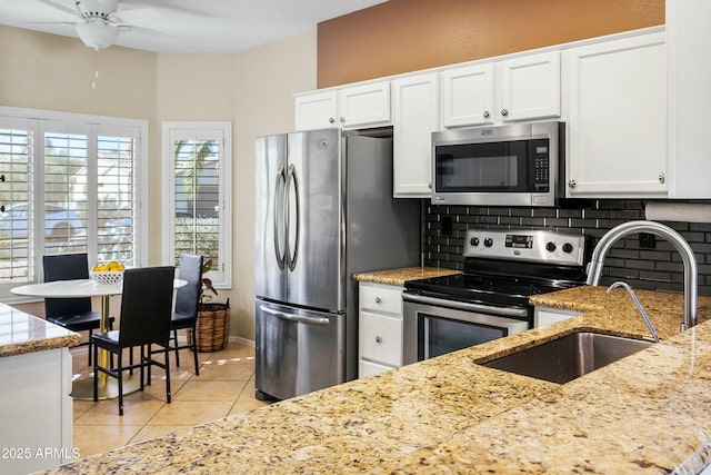 kitchen with appliances with stainless steel finishes, light stone counters, decorative backsplash, white cabinets, and sink