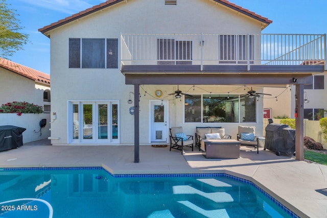 rear view of house with ceiling fan, a balcony, an outdoor living space with a fire pit, and a patio area