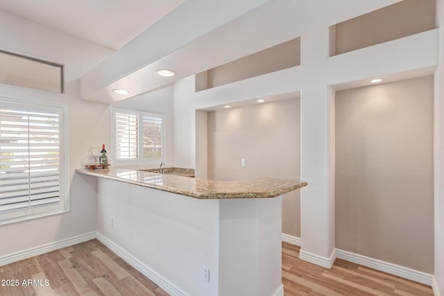 kitchen with light stone countertops, light wood-type flooring, and kitchen peninsula