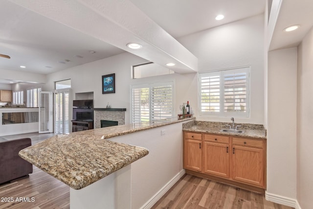 kitchen with a fireplace, light stone countertops, kitchen peninsula, and sink