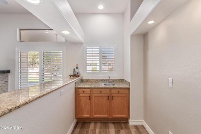 bar with light hardwood / wood-style floors, light stone countertops, sink, and a wealth of natural light