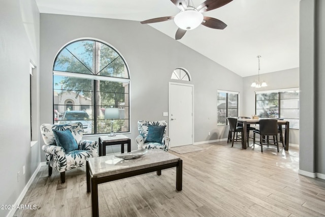 sitting room featuring ceiling fan with notable chandelier, high vaulted ceiling, a healthy amount of sunlight, and light wood-type flooring