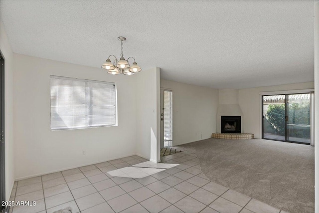 unfurnished living room with light tile patterned floors, an inviting chandelier, a fireplace, a textured ceiling, and light carpet