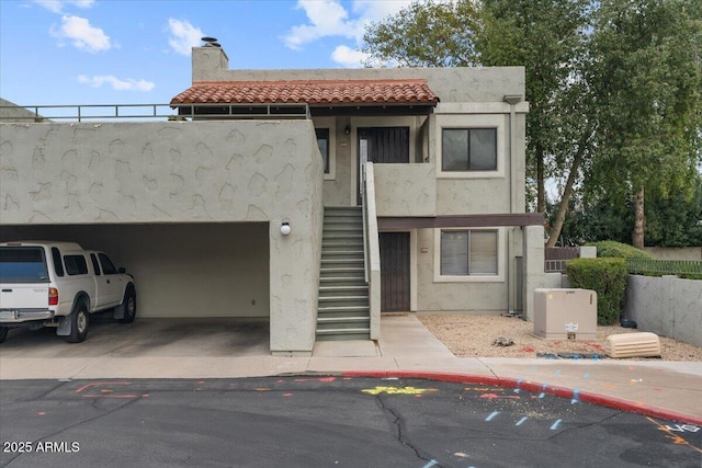 multi unit property featuring stairway, a tile roof, concrete driveway, stucco siding, and a chimney