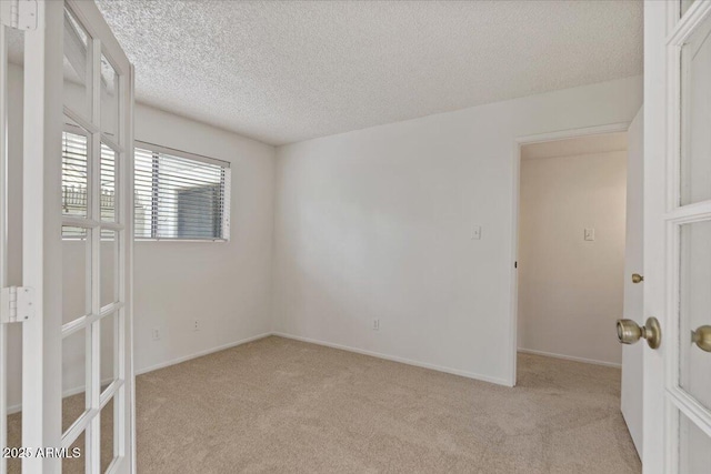 empty room with light carpet, a textured ceiling, and baseboards