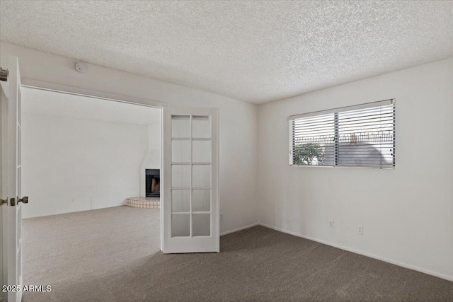 spare room featuring french doors, carpet, a brick fireplace, and a textured ceiling