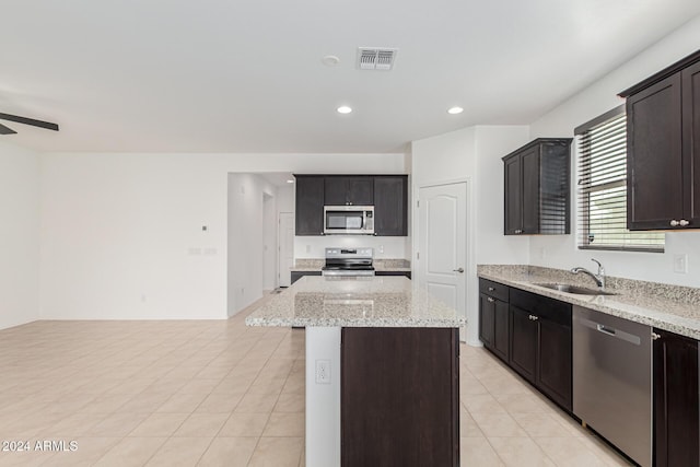 kitchen featuring appliances with stainless steel finishes, light stone counters, ceiling fan, sink, and a center island