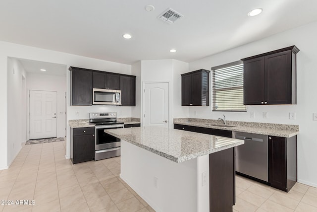 kitchen featuring light stone counters, stainless steel appliances, sink, light tile patterned floors, and a center island