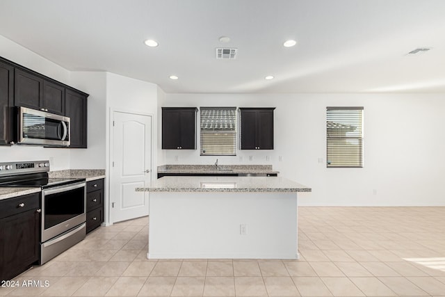 kitchen featuring light stone counters, a center island, stainless steel appliances, and sink