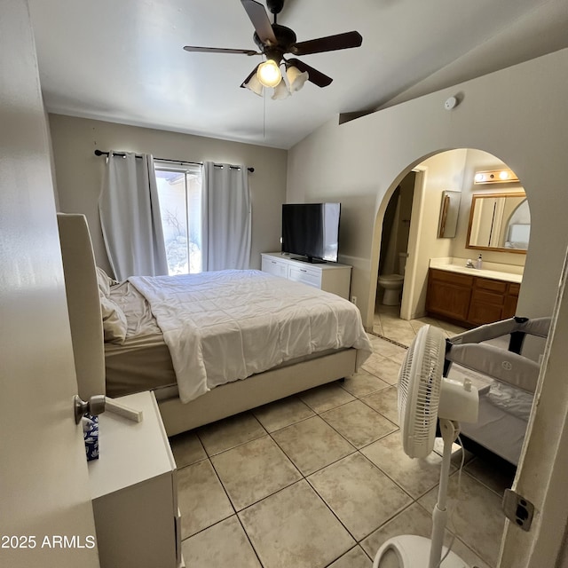 bedroom featuring lofted ceiling, arched walkways, light tile patterned floors, ensuite bathroom, and a sink
