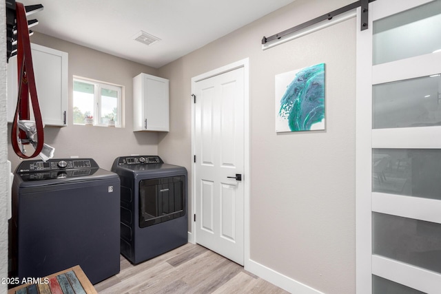 washroom with cabinets, a barn door, washing machine and dryer, and light hardwood / wood-style flooring