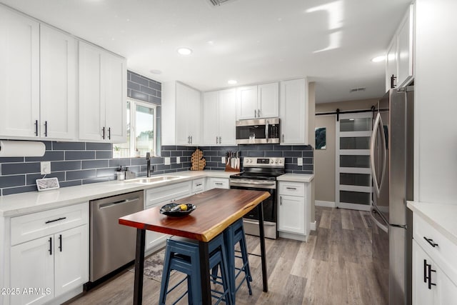 kitchen featuring sink, backsplash, stainless steel appliances, white cabinets, and a barn door