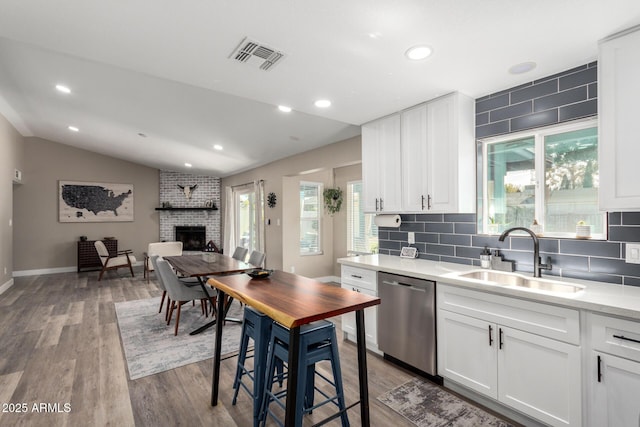 kitchen featuring lofted ceiling, sink, a fireplace, white cabinets, and stainless steel dishwasher