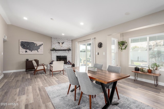 dining room with vaulted ceiling, a brick fireplace, and light hardwood / wood-style flooring