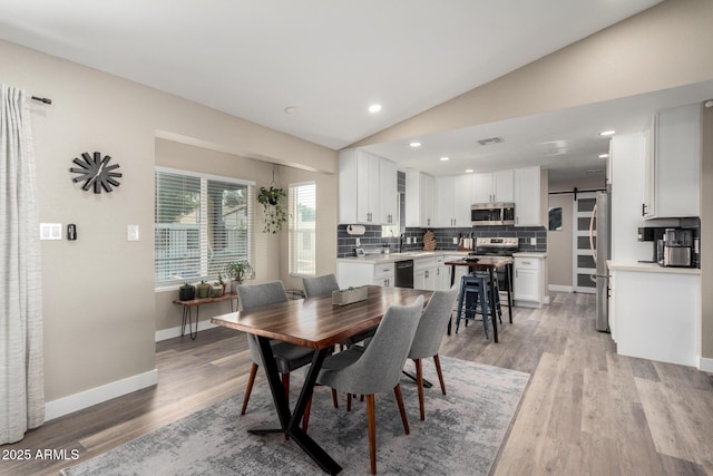 dining space featuring lofted ceiling, sink, light hardwood / wood-style floors, and a barn door