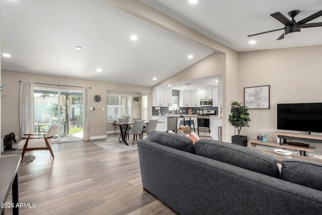 living room with ceiling fan, lofted ceiling, and light hardwood / wood-style floors