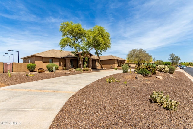 ranch-style house with concrete driveway, a tile roof, fence, and stucco siding