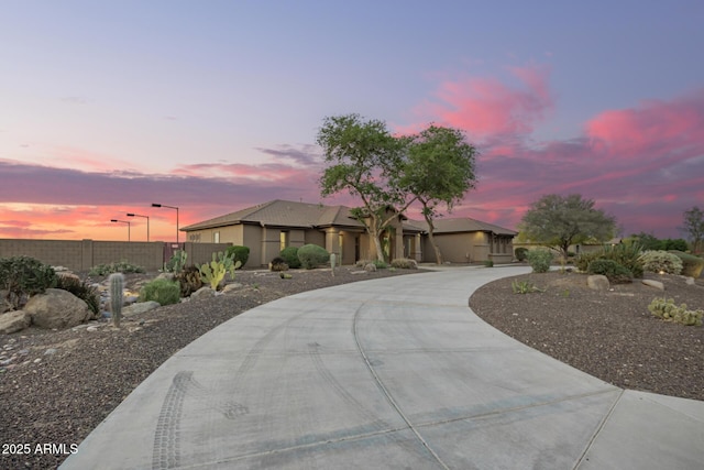 single story home with stucco siding, fence, and curved driveway