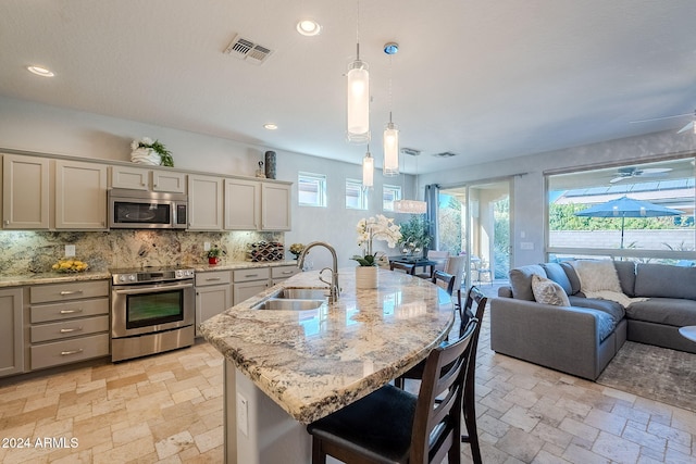 kitchen featuring sink, hanging light fixtures, stainless steel appliances, an island with sink, and decorative backsplash