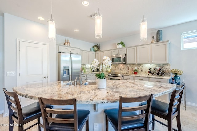 kitchen with a kitchen island with sink, hanging light fixtures, decorative backsplash, and stainless steel appliances