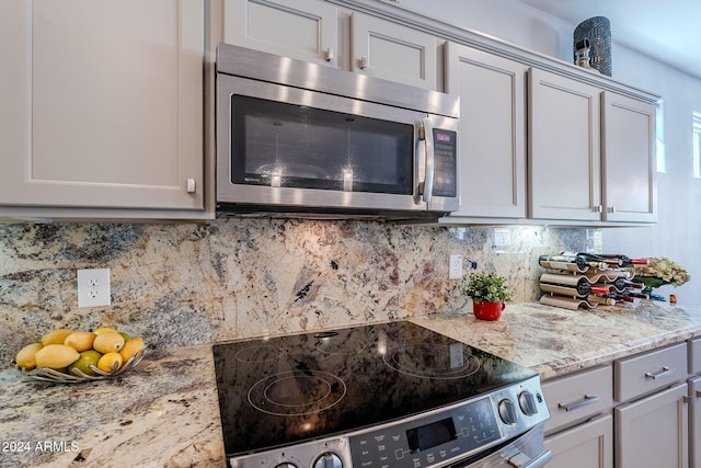 kitchen with appliances with stainless steel finishes, light stone countertops, decorative backsplash, and gray cabinetry