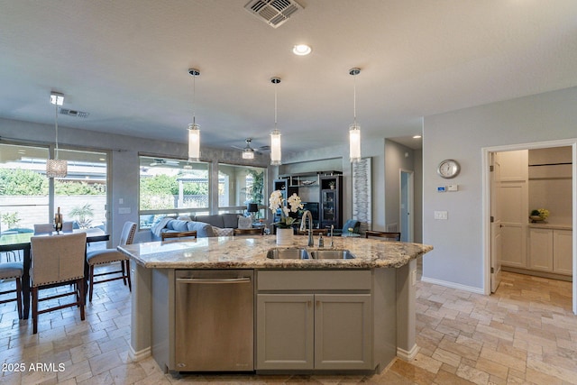 kitchen featuring hanging light fixtures, sink, a center island with sink, and light stone counters