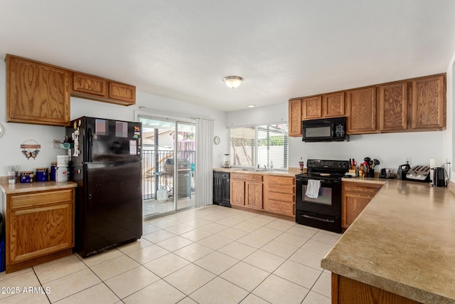 kitchen featuring brown cabinetry, light tile patterned floors, light countertops, a sink, and black appliances