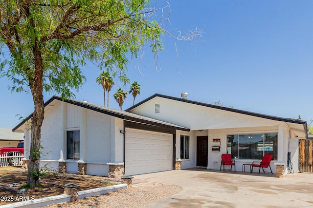 ranch-style house with driveway, a garage, fence, stone siding, and stucco siding