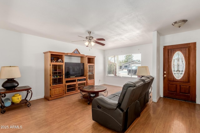 living area with baseboards, a ceiling fan, and light wood-type flooring