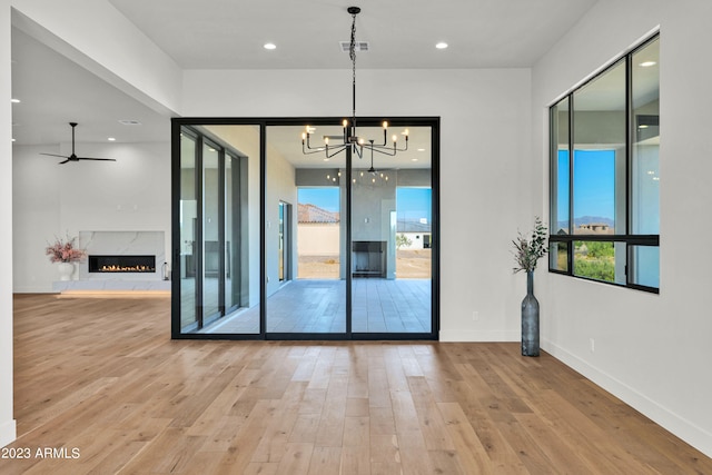 doorway to outside with a fireplace, ceiling fan with notable chandelier, and light wood-type flooring