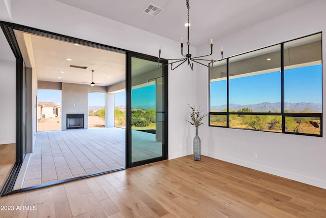 spare room with a chandelier, light wood-type flooring, and a wealth of natural light