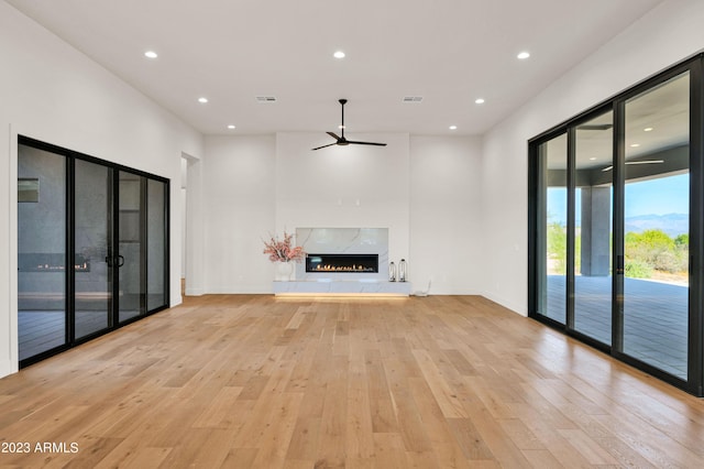 unfurnished living room featuring light hardwood / wood-style flooring, ceiling fan, a premium fireplace, and french doors