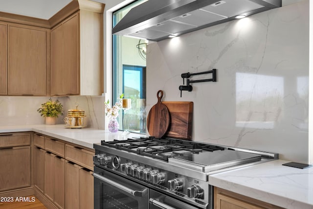 kitchen with light stone countertops, backsplash, wall chimney range hood, and double oven range