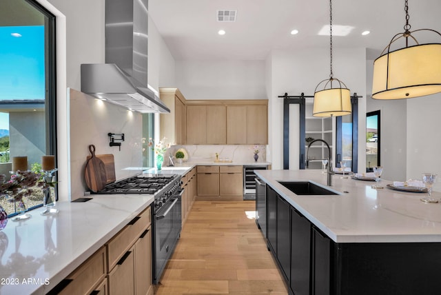 kitchen featuring a barn door, double oven range, light hardwood / wood-style floors, wall chimney exhaust hood, and tasteful backsplash