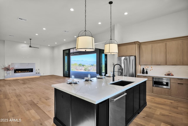 kitchen with decorative light fixtures, light hardwood / wood-style floors, stainless steel appliances, an island with sink, and a high end fireplace