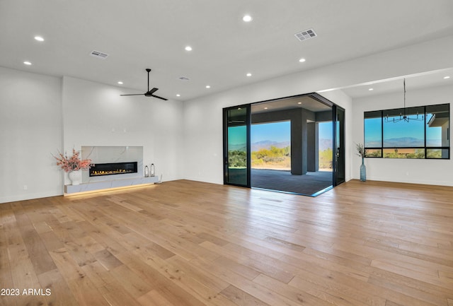 unfurnished living room featuring a fireplace, ceiling fan with notable chandelier, light wood-type flooring, and plenty of natural light