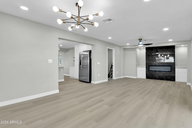 unfurnished living room with ceiling fan with notable chandelier, light hardwood / wood-style floors, and a tiled fireplace