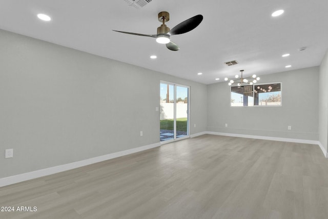 empty room with ceiling fan with notable chandelier and light hardwood / wood-style floors