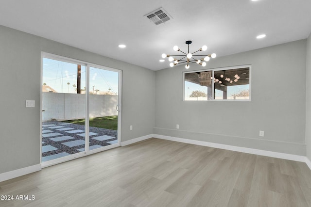 spare room featuring a chandelier, light wood-type flooring, and plenty of natural light