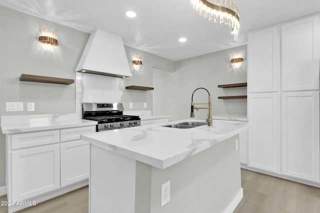 kitchen with premium range hood, a kitchen island with sink, sink, white cabinets, and stainless steel gas stove