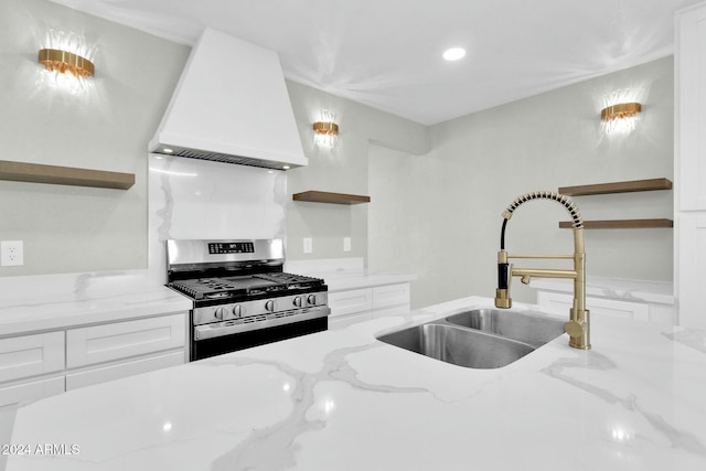 kitchen with sink, gas range, custom range hood, light stone counters, and white cabinetry