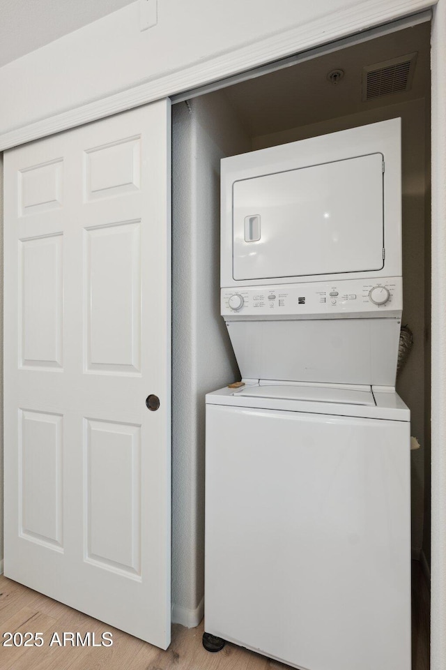 laundry area with stacked washer and dryer, laundry area, visible vents, and light wood-style floors