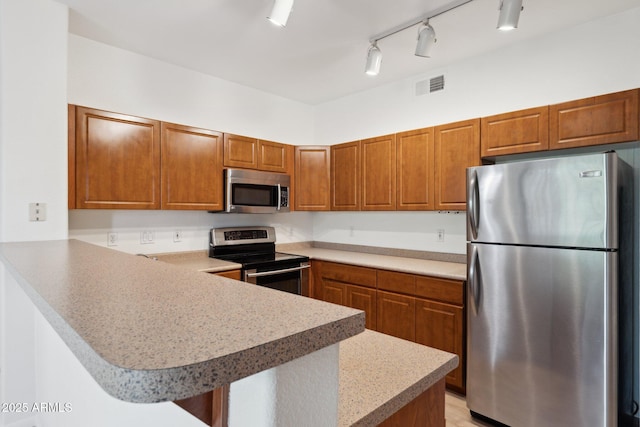 kitchen featuring light countertops, brown cabinetry, stainless steel appliances, a peninsula, and visible vents