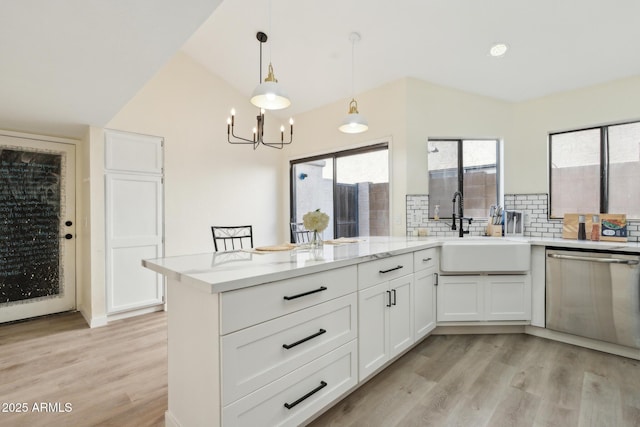 kitchen with stainless steel dishwasher, a sink, light wood finished floors, decorative backsplash, and a chandelier