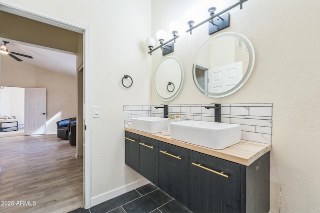 bathroom featuring ceiling fan, vaulted ceiling, double vanity, and baseboards