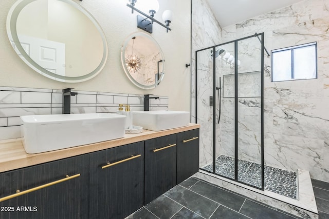 bathroom featuring a marble finish shower, double vanity, and tile walls
