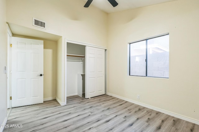 unfurnished bedroom with wood finished floors, baseboards, a closet, a towering ceiling, and a ceiling fan