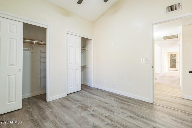 unfurnished bedroom with two closets, wood finished floors, baseboards, vaulted ceiling, and ceiling fan