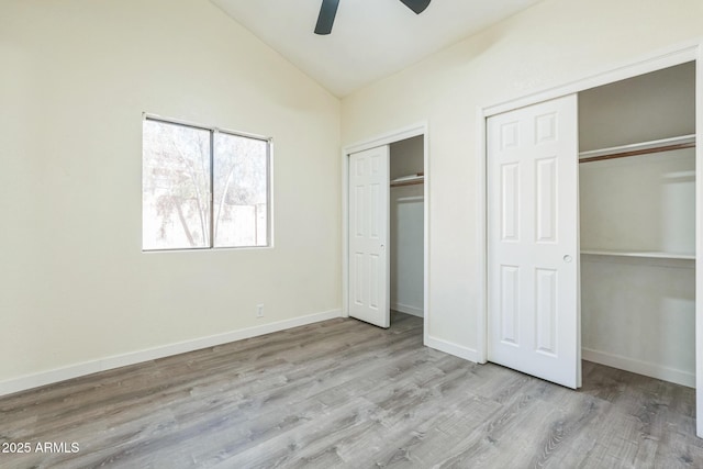 unfurnished bedroom with two closets, lofted ceiling, wood finished floors, baseboards, and a ceiling fan