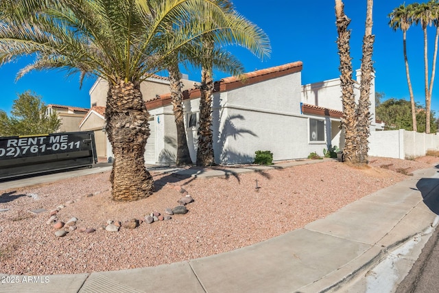 view of front of property featuring stucco siding, a tiled roof, and fence